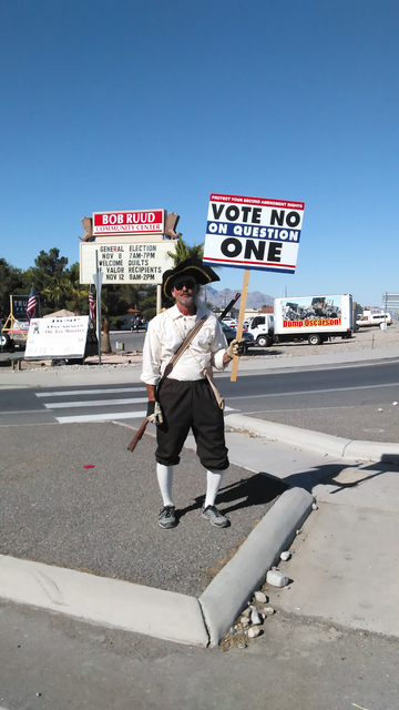 A man dressed as a Revolutionary War-era militia man near the polling place at Bob Ruud Community Center encourages voters to note no on State Ballot Question 1 which would expand background check ...