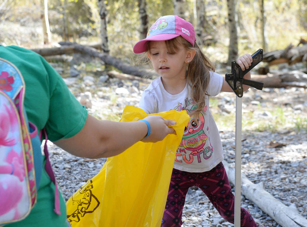 Jenna Harris, 5, from Girl Scout Troop 518 places up a piece of trash off the ground into a garbage bag while participating in the litter collection as a part of the volunteer program called &quot ...