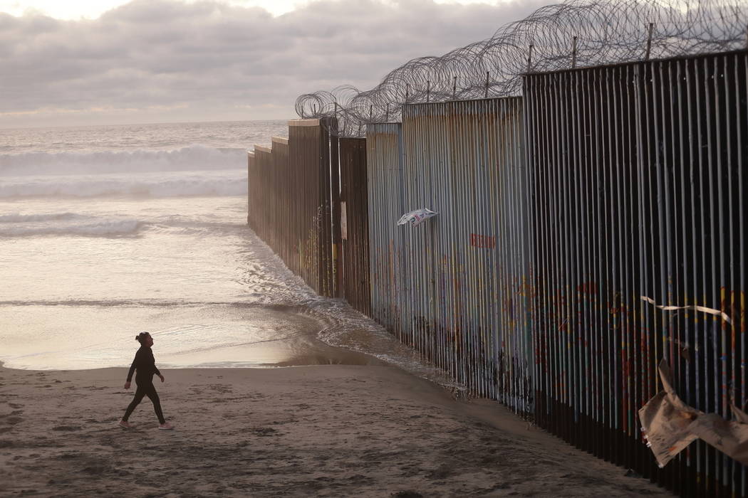 A woman walks on the beach next to the border wall topped with razor wire in Tijuana, Mexico, in January 2019. (AP Photo/Gregory Bull)