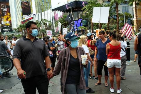 Visitors to the Las Vegas Strip, wearing masks to prevent the spread of COVID-19, pass a group ...