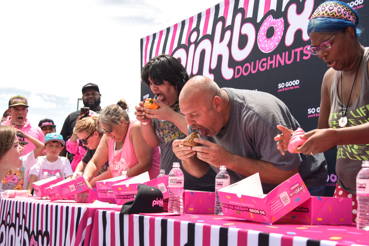 The adult eating contest begins with big bites at the grand opening of the Pinkbox Doughnuts sh ...