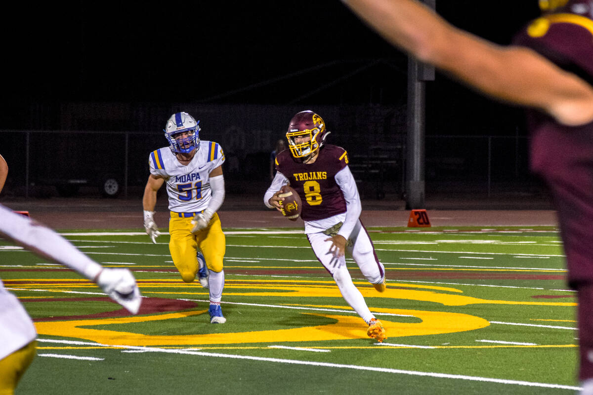 Trojan’s Kayne Horibe (8) chased by Moapa Valley after nearly being sacked looks for an ...