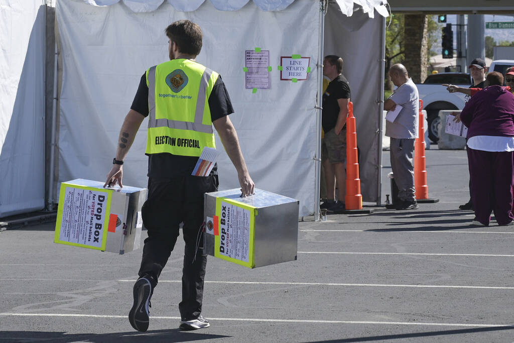 An election official carries empty ballot drop boxes to a polling place on Blue Diamond Road on ...