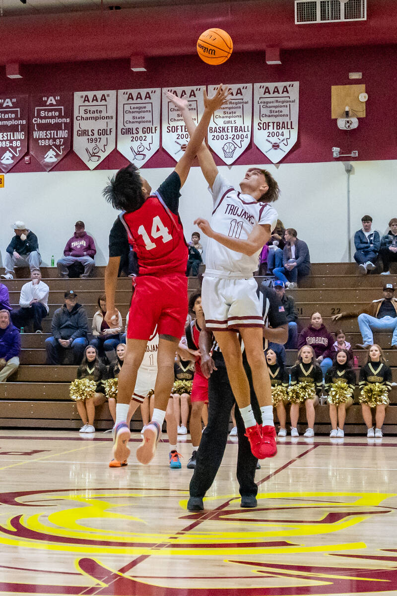 Trojans junior Aydon Veloz (11) (right) and Dragons freshman Kobe Artadi (14) (left) both jump ...