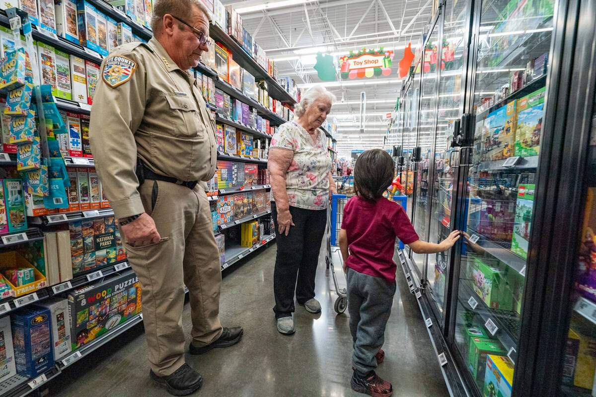 Sheriﬀ Joe McGill and his assigned kid and his foster parent inspect the Legos in the toy ais ...