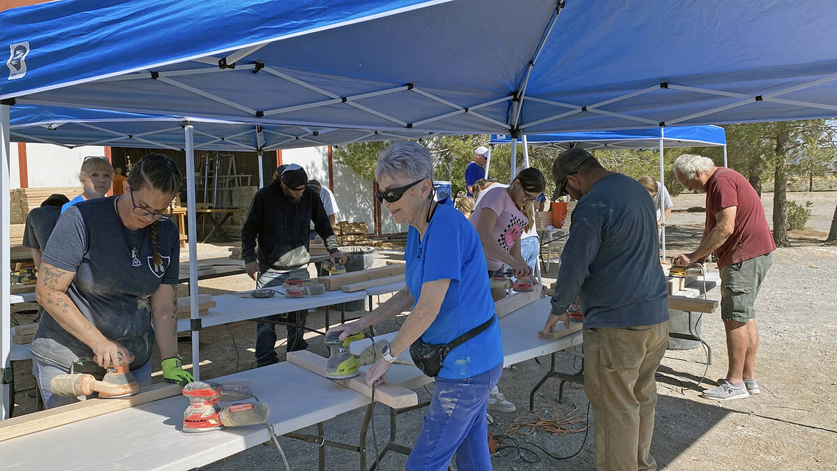 With pop-up tents to provide much-needed shade, volunteers work to sand lengths of lumber at th ...